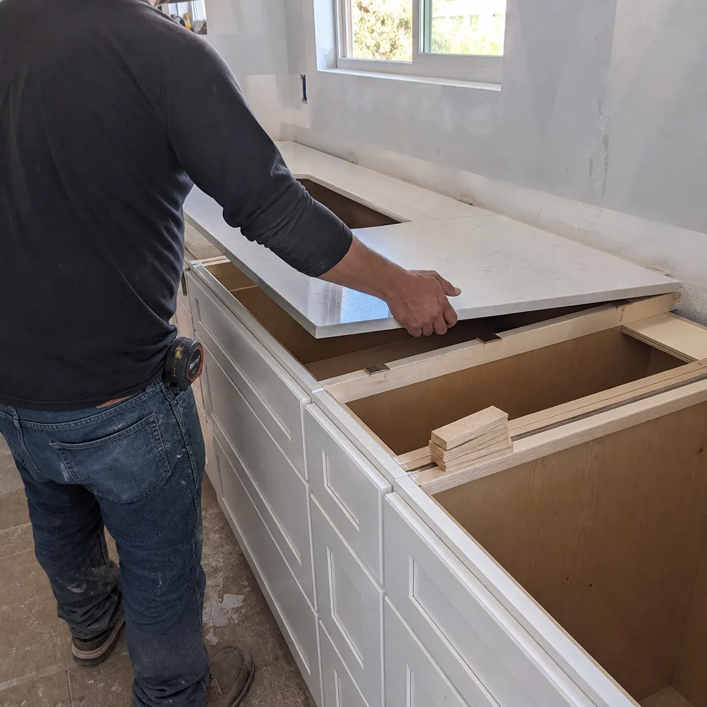 Contractor installing quartz kitchen countertop on white cabinets